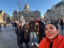 Group of six people smiling in city square on a sunny day.