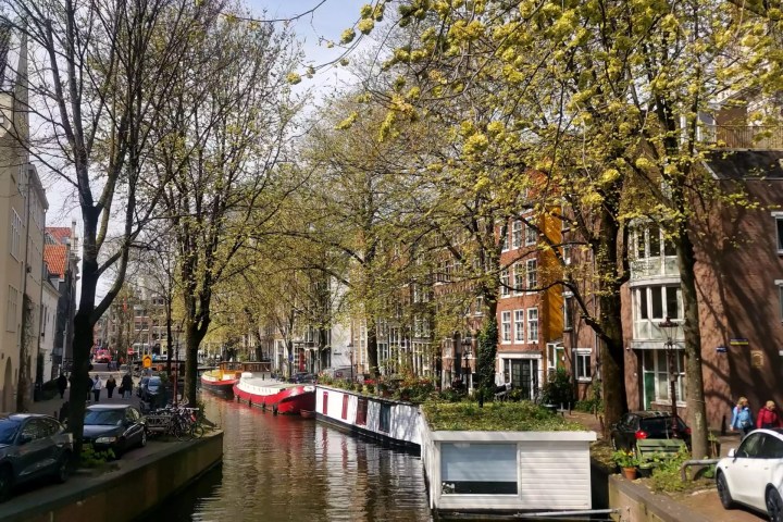 photo of a canal in amsterdam city centre in daylight, house boats, people walking on the canal banks