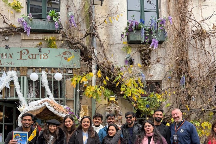 Group posing outside a rustic building with greenery and flowers.