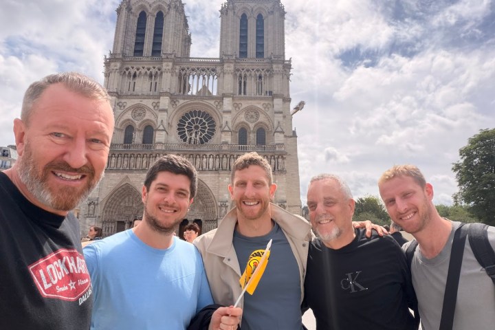 Five men smiling in front of Notre-Dame Cathedral, under a cloudy sky.