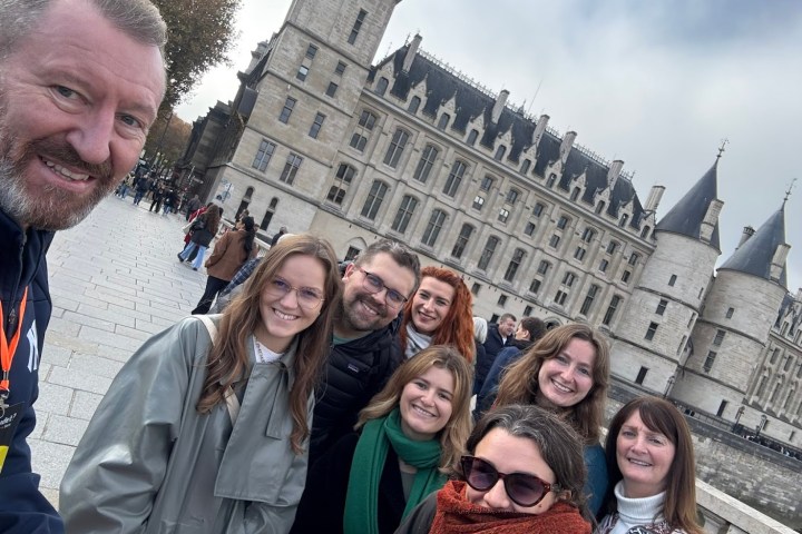 Group of people smiling in front of a historic building on a cloudy day.