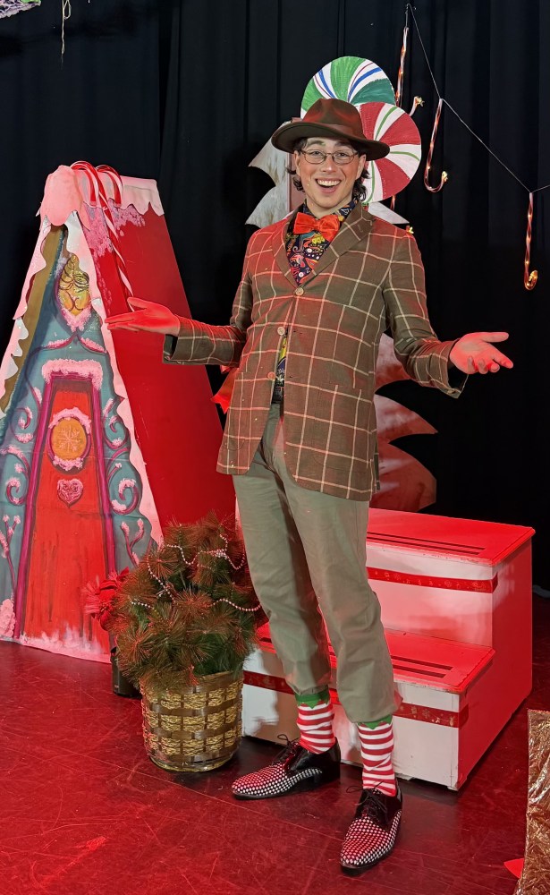 Person in festive outfit with striped socks and hat, standing by colorful holiday decorations.