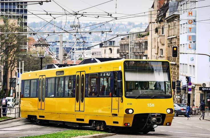 Yellow tram on city street with buildings and overhead wires.