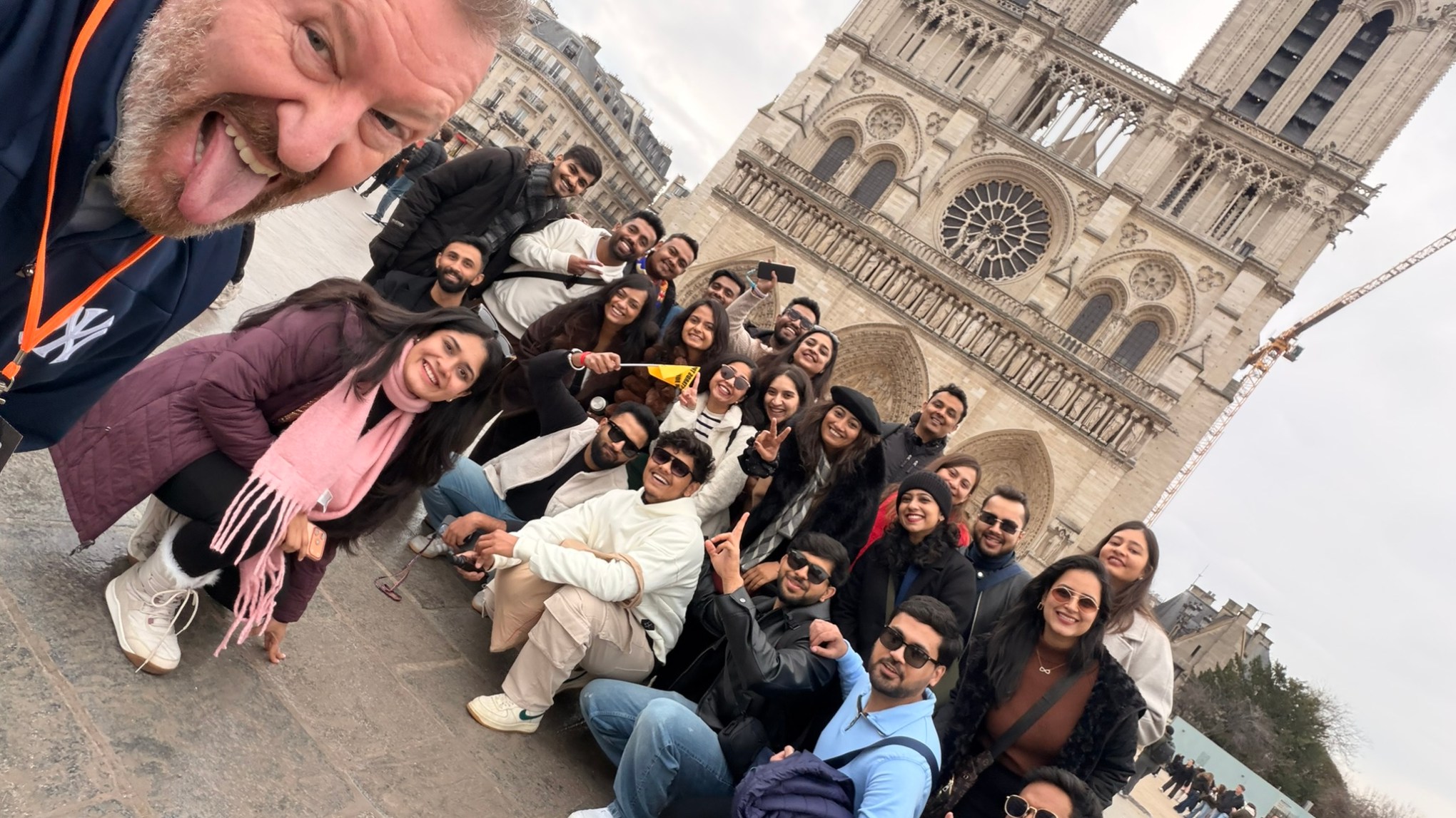 Group photo in front of Notre-Dame Cathedral, Paris, with selfie taken by a man on the left.