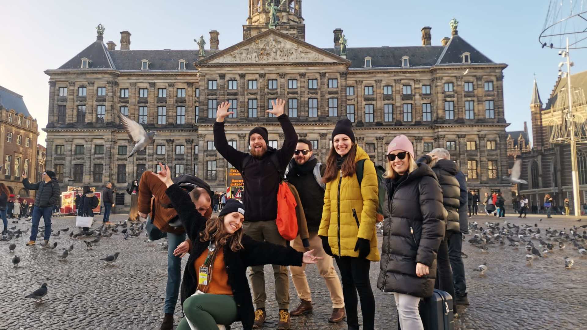 Group of people posing happily in front of a historic building with pigeons around.