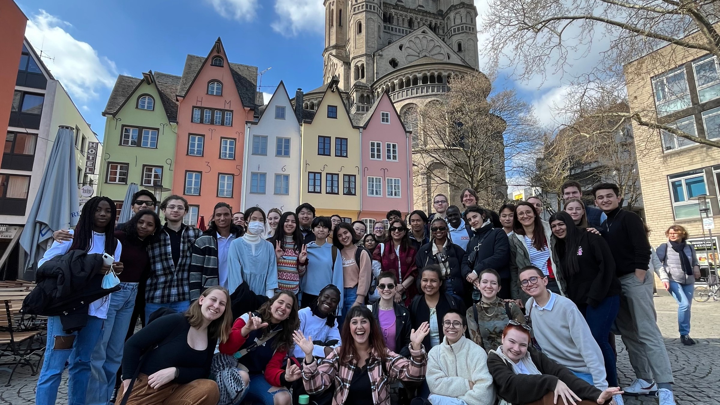 Group of people posing in front of colorful buildings and a church on a cobblestone street.