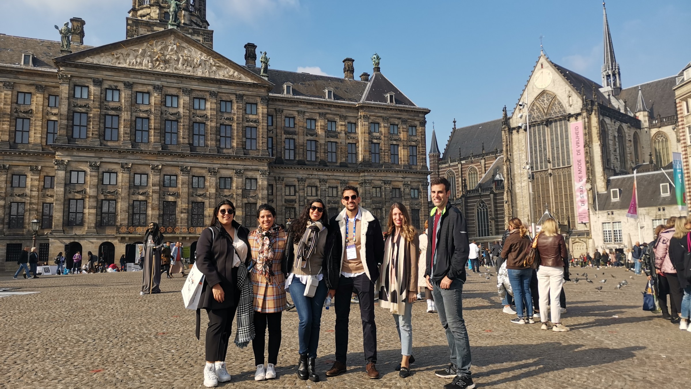 Group of six people posing in front of historic buildings in a plaza.