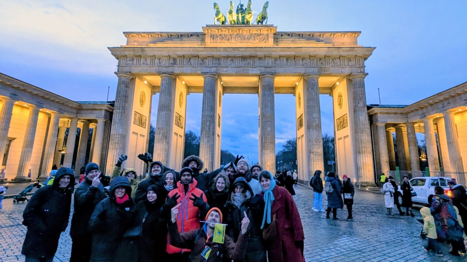 Group of people posing in front of the illuminated Brandenburg Gate at dusk.