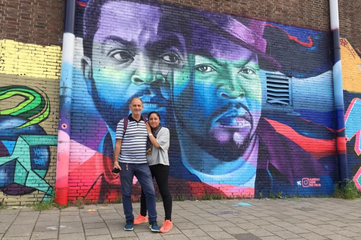 Couple posing in front of colorful street art on brick wall.