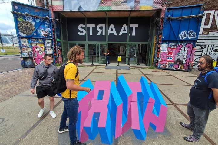 People stand around 3D 'TRUTH' art outside a building with 'STRAAT' sign.