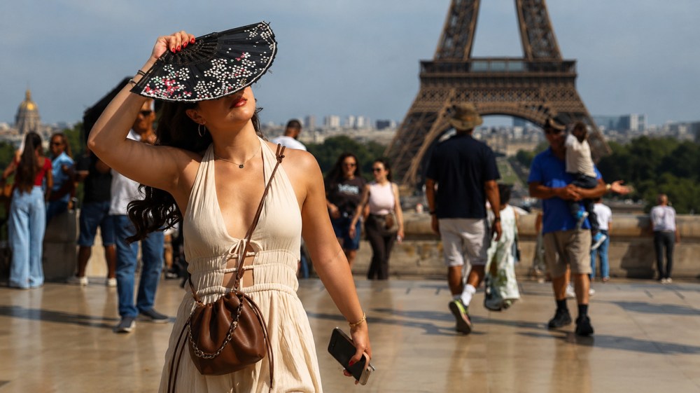 Woman shielding face with fan near Eiffel Tower, Paris.