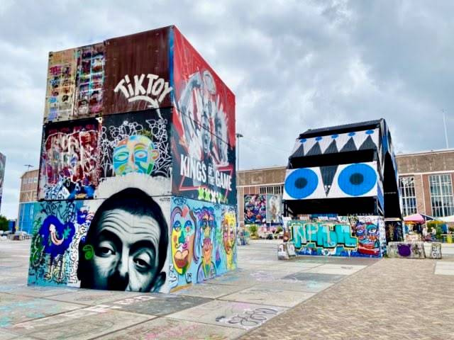Colorful graffiti-covered cube structures in urban setting under cloudy sky.
