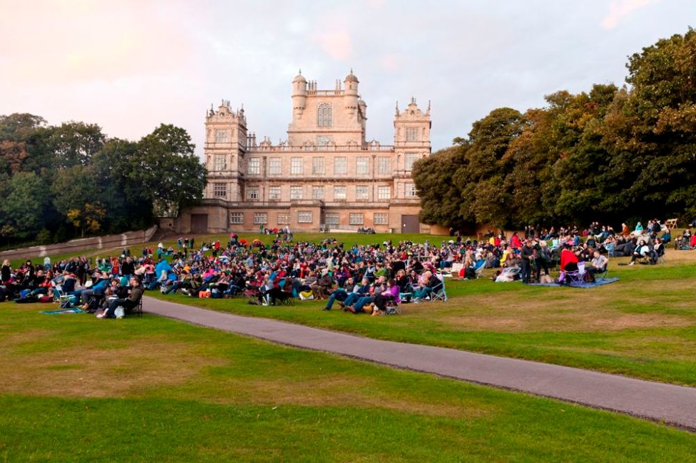 Large crowd seated on lawn in front of a historic mansion.