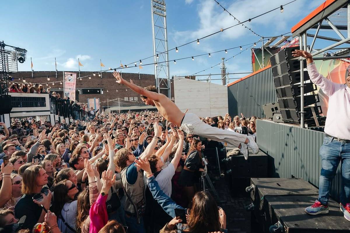 Man crowd surfing over cheering audience at an outdoor concert.