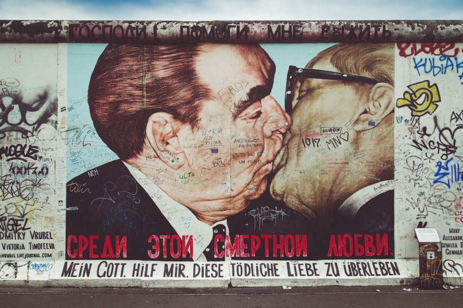 Famous mural of two men kissing on Berlin Wall, covered in graffiti.