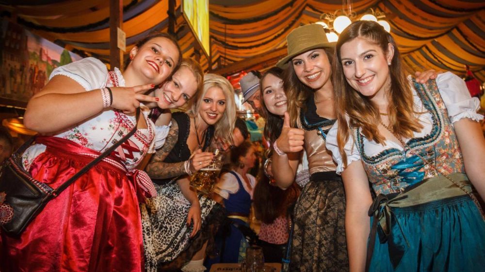 Group of smiling women in festive traditional dresses at an event.