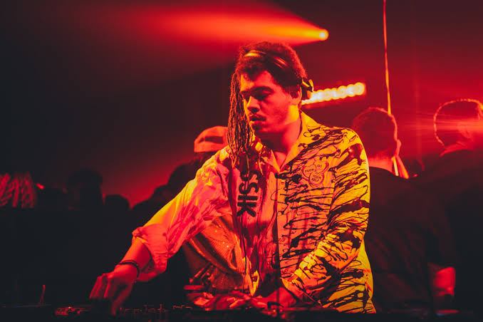 DJ performing on stage with red lighting.