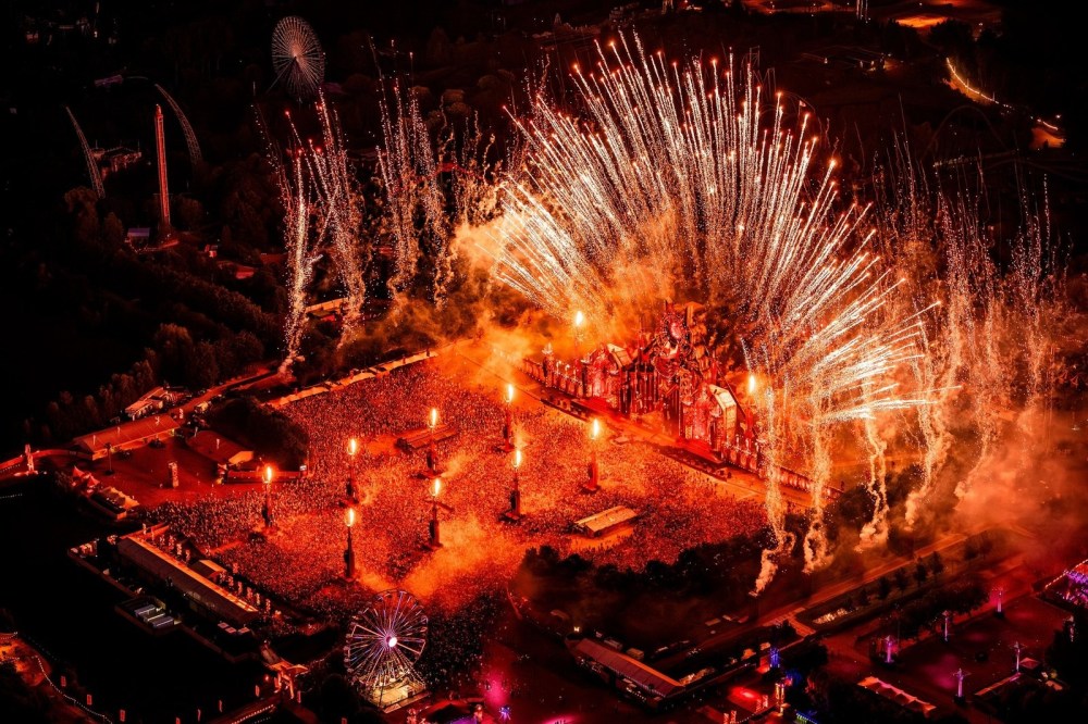 Aerial view of a large outdoor concert with fireworks lighting up the night sky.